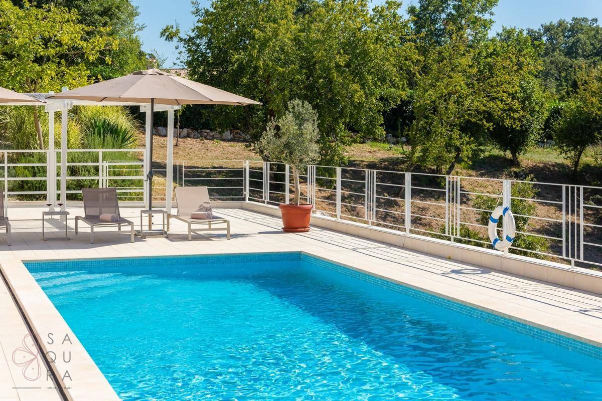 Heller Poolbereich mit Liegestühlen und einem Rettungsring, umgeben von Grün.