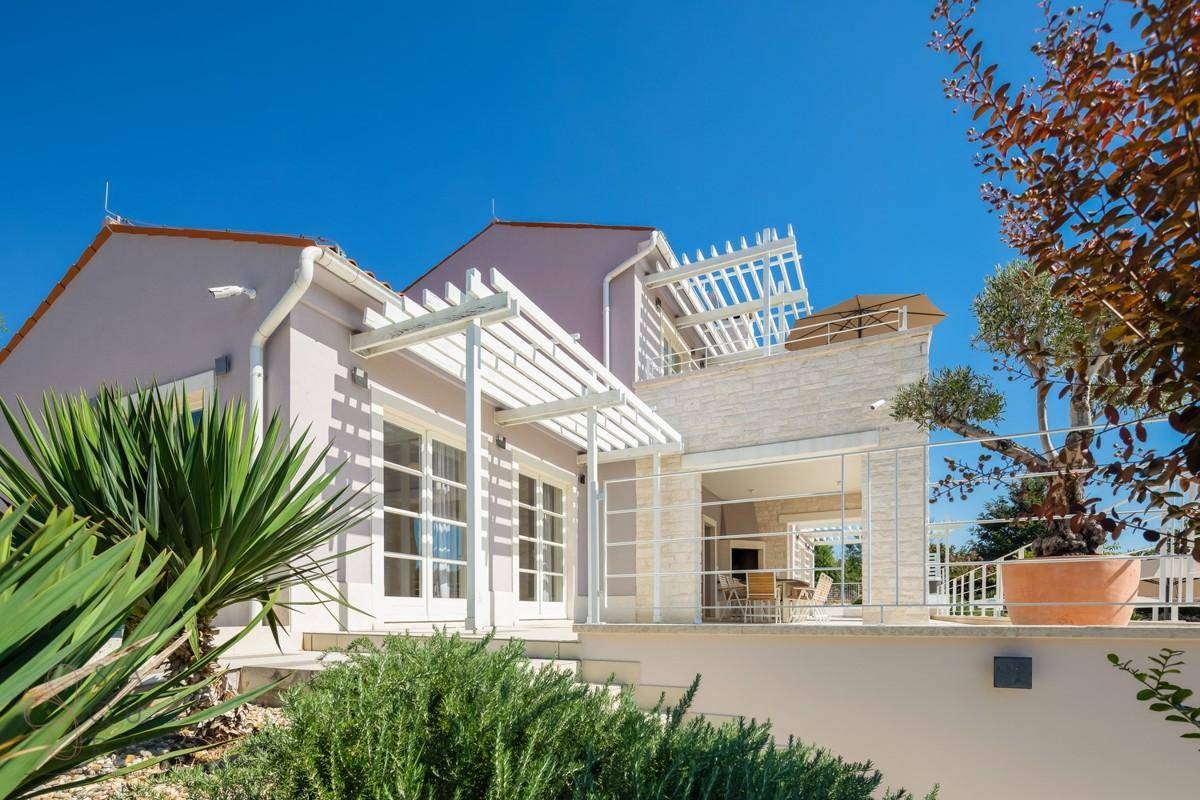 Moderne Villa mit Terrassenbereich, Pergola und üppiger mediterraner Bepflanzung.