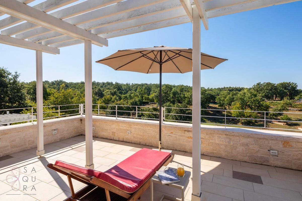 Sonnige Terrasse mit Liegestuhl und Sonnenschirm, umgeben von üppigem Grün und weitem Blick.