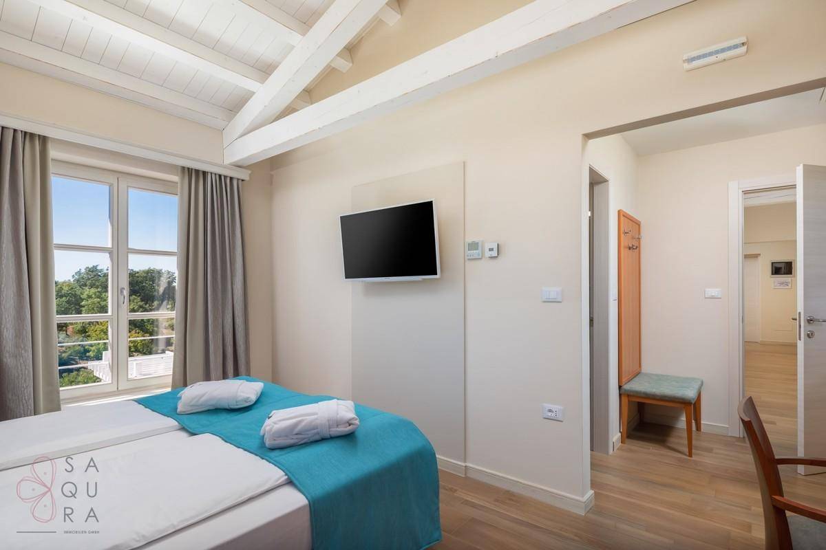 Helles Schlafzimmer mit zwei Einzelbetten, Flachbildfernseher und Zugang zu einem weiteren Raum.