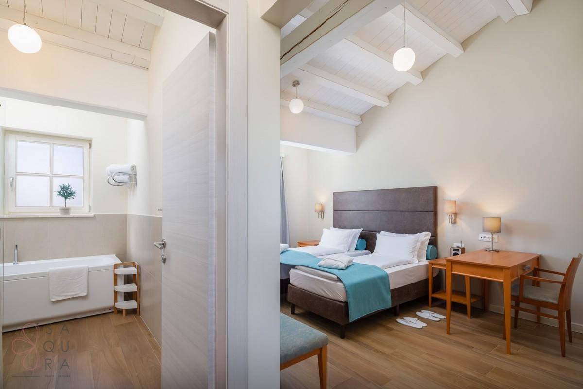 Innenansicht mit einem Schlafzimmer und einem angrenzenden Badezimmer, beide mit Holzboden.