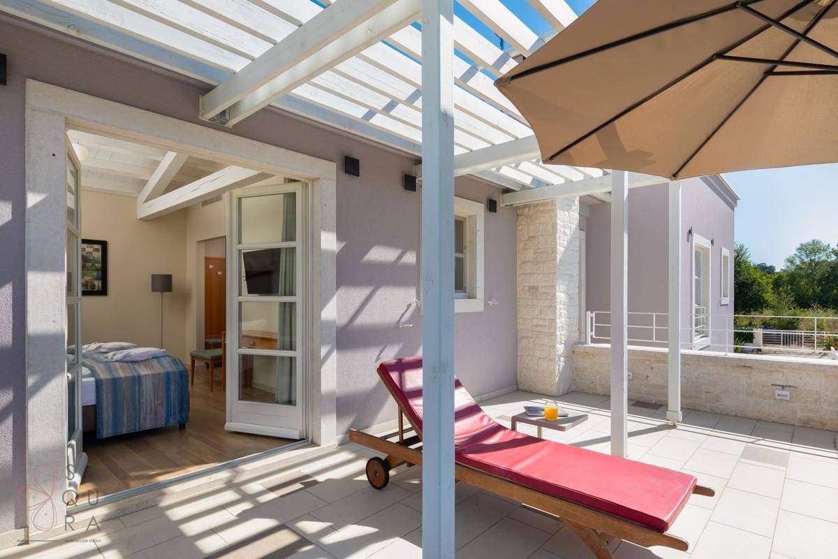 Geräumige Terrasse mit Liegestuhl und Sonnenschirm, direkter Zugang zu einem hellen Schlafzimmer.