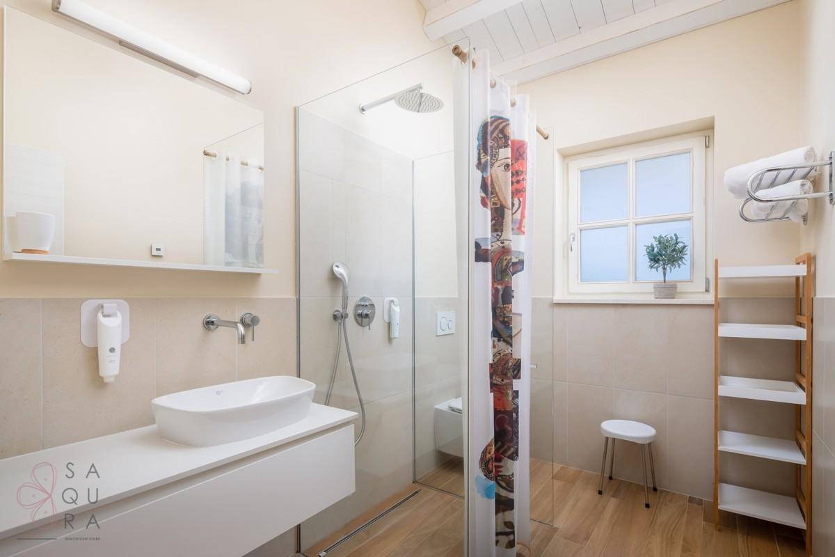 Modernes Badezimmer mit ebenerdiger Dusche, Waschbecken und Fenster für Tageslicht.