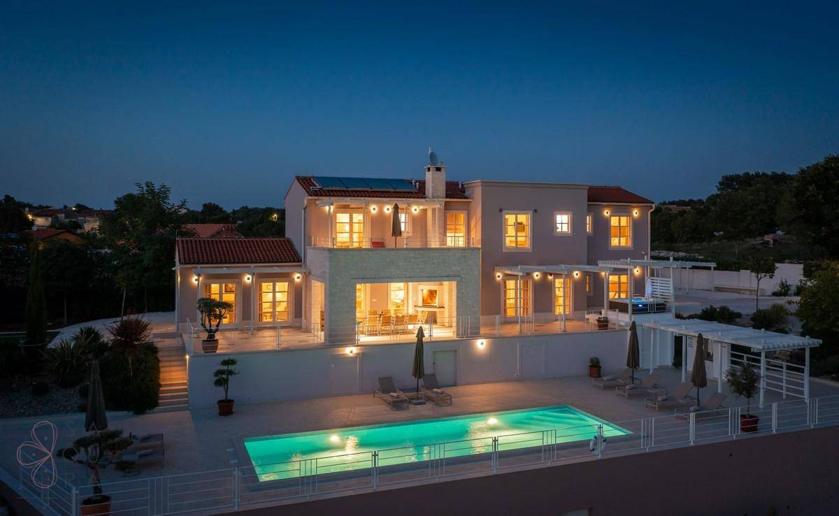 Elegante Villa mit großem Poolbereich und stilvoller Außenbeleuchtung in der Abenddämmerung.