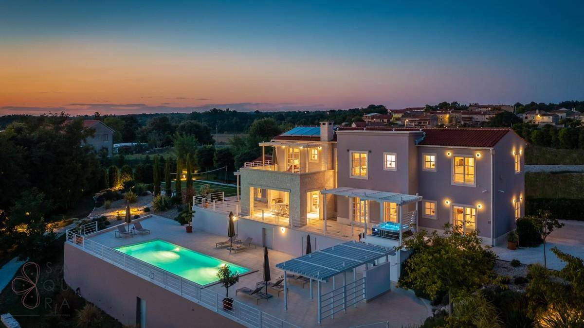 Luxuriöse Villa mit beleuchtetem Pool und weitläufiger Terrasse bei Einbruch der Dunkelheit.