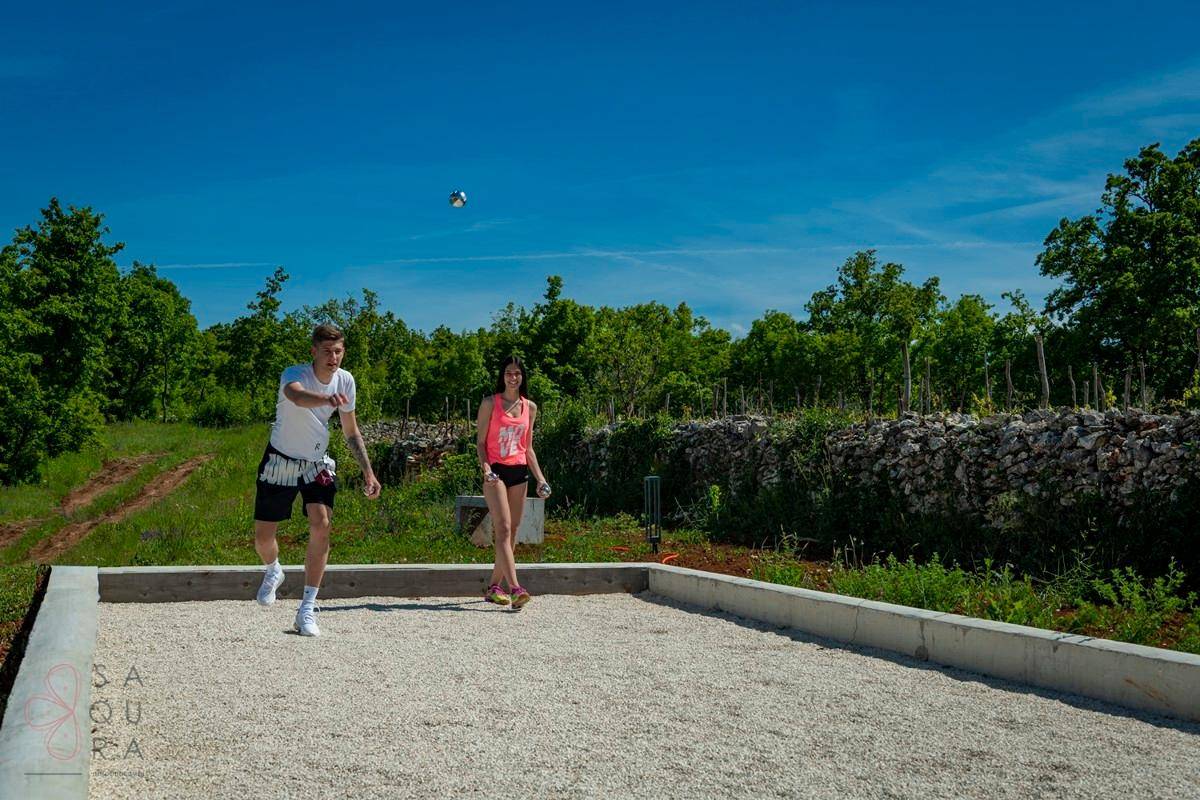 Außenbereich mit einem Boccia-Platz, umgeben von grüner Landschaft unter blauem Himmel.