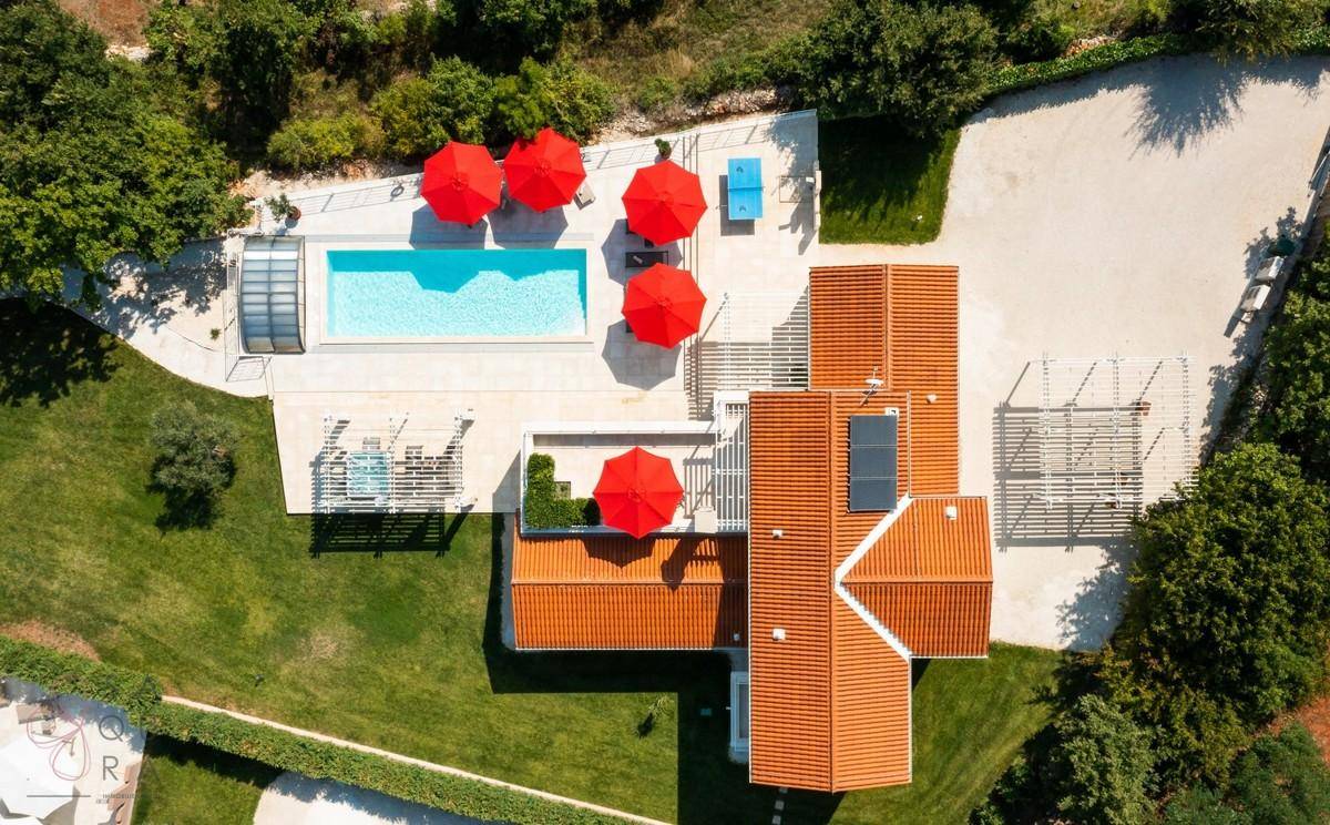 Vogelperspektive der Villa mit Pool, Sonnenschirmen und Photovoltaikanlage auf dem Dach.