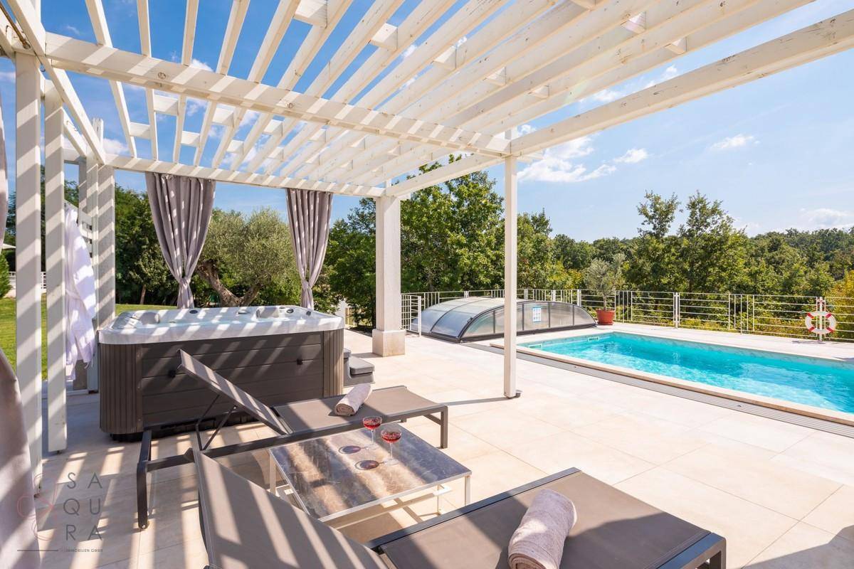 Entspannungsbereich mit Whirlpool und Liegestühlen unter einer Pergola, neben dem erfrischenden Pool.