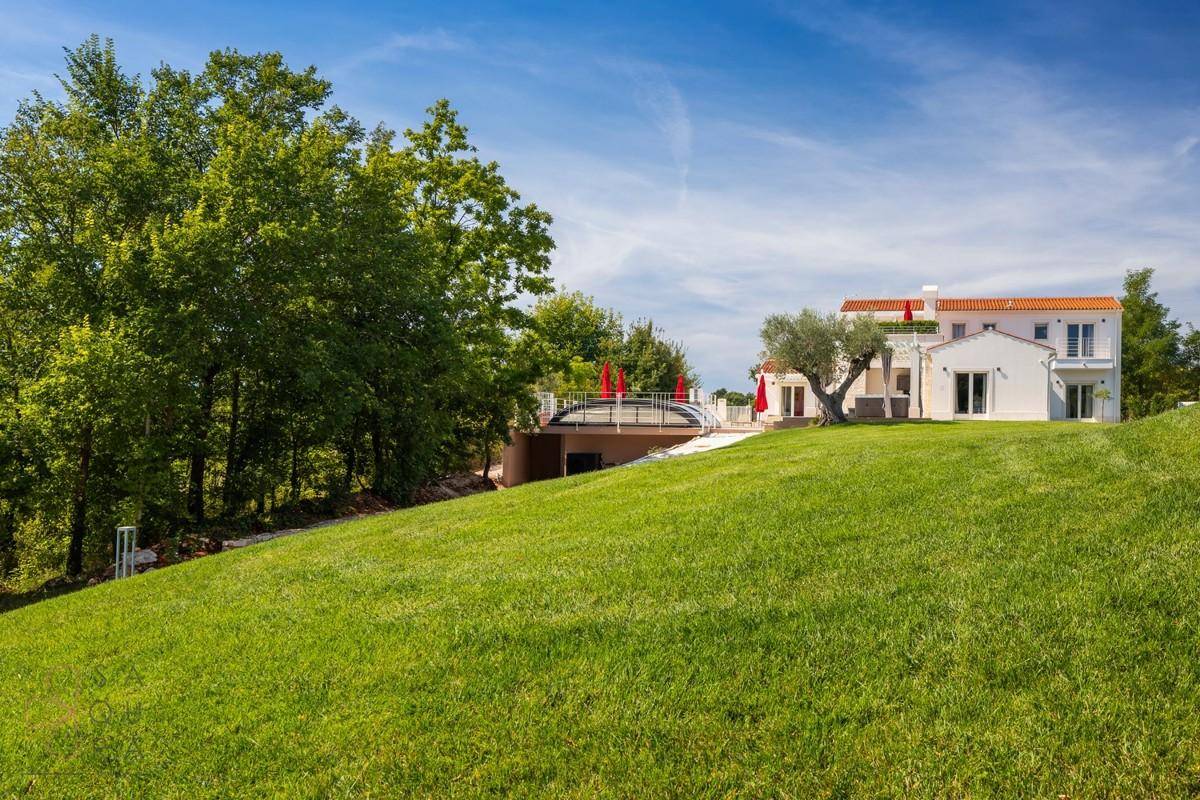 Große Rasenfläche mit Blick auf die Villa und den Poolbereich im Hintergrund, umgeben von Bäumen.