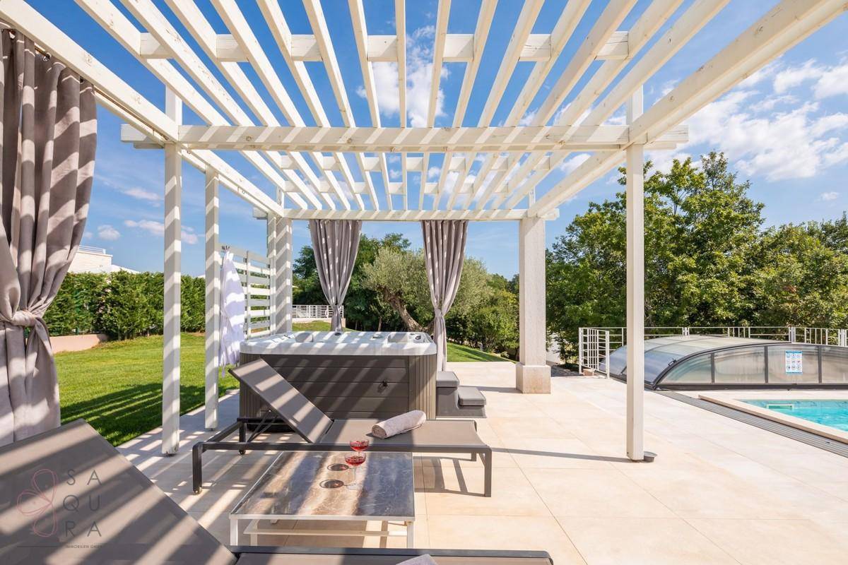 Entspannungsbereich mit Whirlpool unter einer schattenspendenden Pergola und bequemen Liegestühlen.