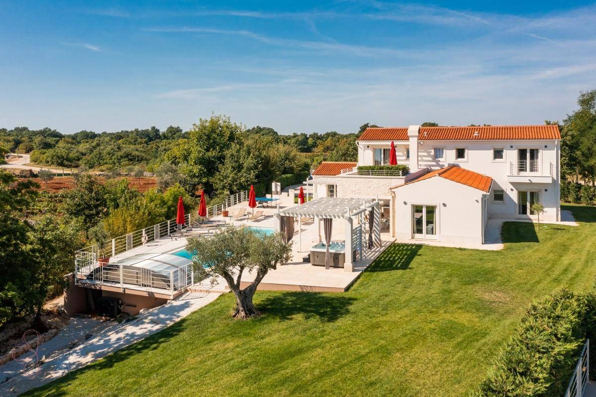 Weitläufige Ansicht der Villa mit Pool, Garten und Blick auf die umliegende grüne Landschaft.