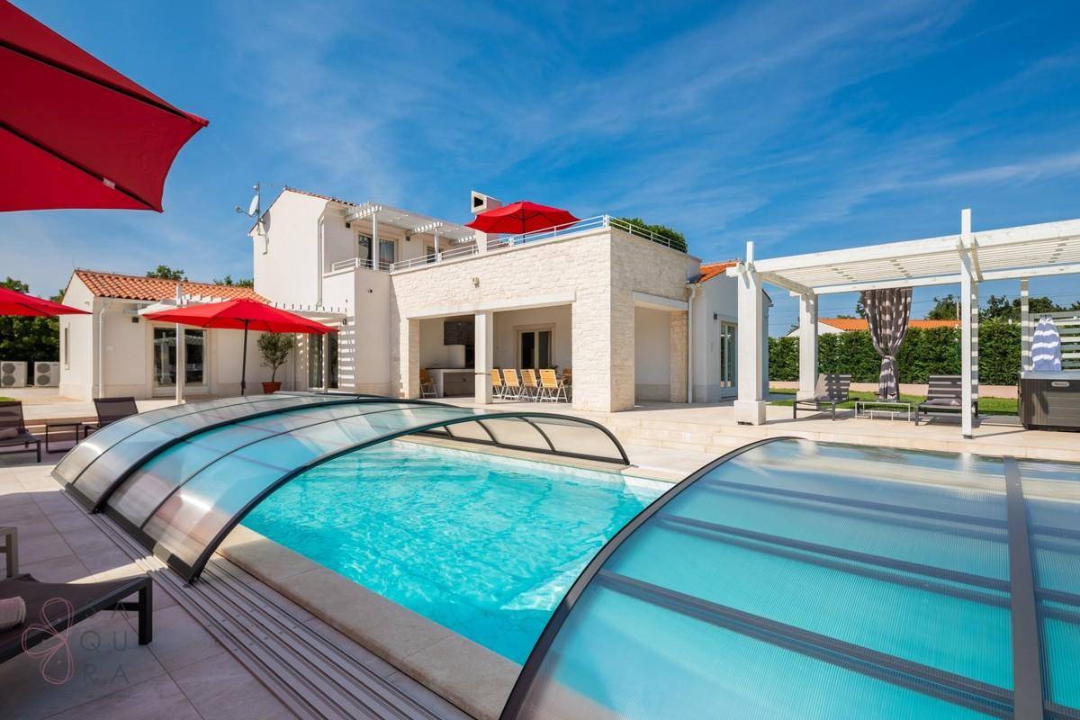 Der Pool mit transparenter Abdeckung, umgeben von Liegeflächen und der modernen Villa.