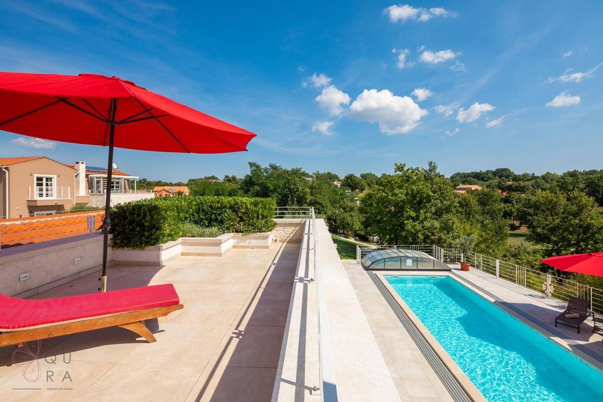Dachterrasse mit Sonnenliege und weitem Blick über die grüne Landschaft und den Poolbereich.