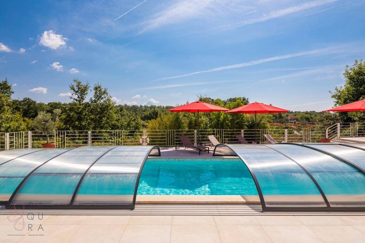 Pool mit transparenter Abdeckung und Liegeflächen, mit weitem Blick auf die grüne Landschaft.