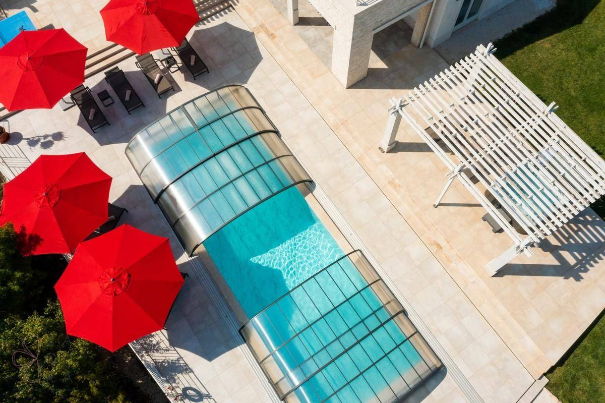 Luftaufnahme des Pools mit transparenter, ausziehbarer Abdeckung und umliegenden Liegeflächen.