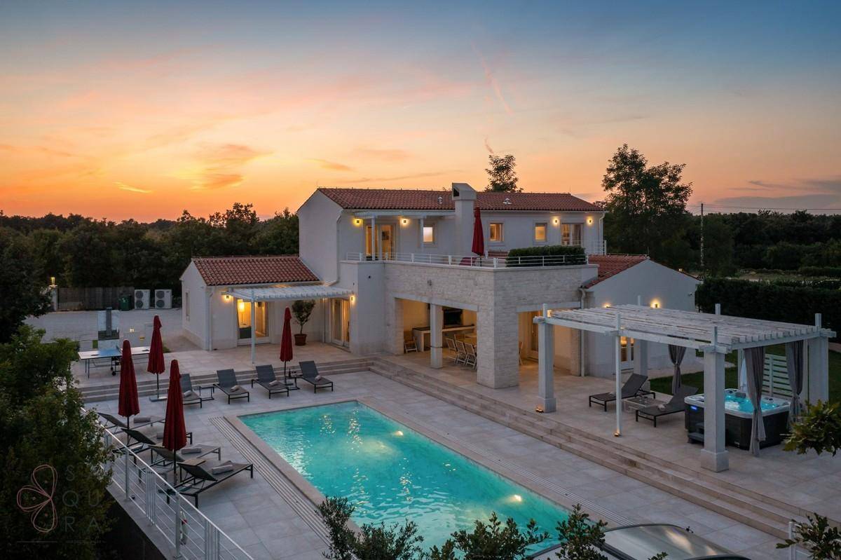 Weitläufige Außenansicht der Villa mit großem Pool, Whirlpool und weitläufiger Landschaft bei Sonnenuntergang.