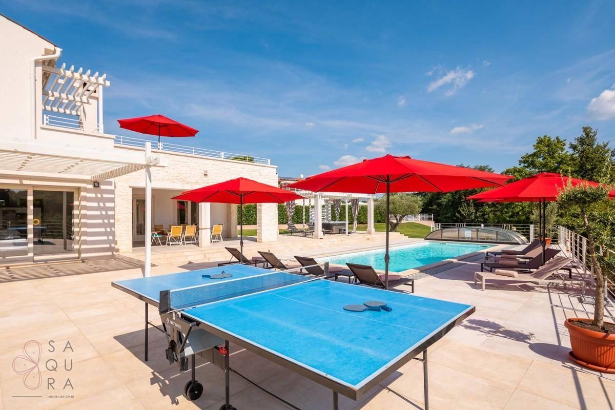 Weitläufiger Poolbereich mit Tischtennisplatte, Liegestühlen und Blick auf die moderne Villa.