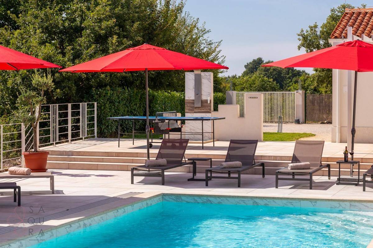 Poolbereich mit Liegestühlen, Sonnenschirmen und einer Tischtennisplatte für Freizeitaktivitäten.