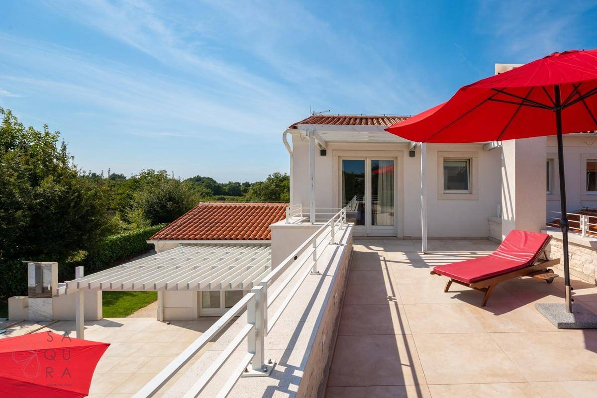 Geräumige Dachterrasse mit Blick auf die moderne Architektur der Villa und die Pergola im Garten.