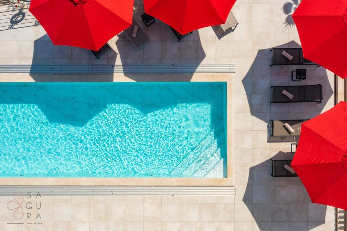 Draufsicht auf den rechteckigen Pool mit klarem Wasser und den umliegenden Liegebereich.