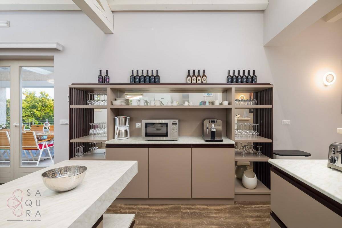 Küchenzeile mit Kaffeemaschine, Mikrowelle und eleganten Regalen für Geschirr und Flaschen.