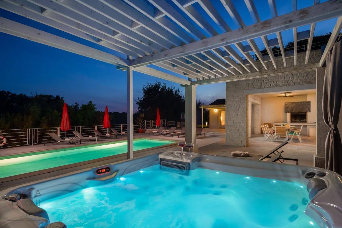 Beleuchteter Whirlpool und überdachter Essbereich im Freien bei Nacht mit Blick auf den Pool.