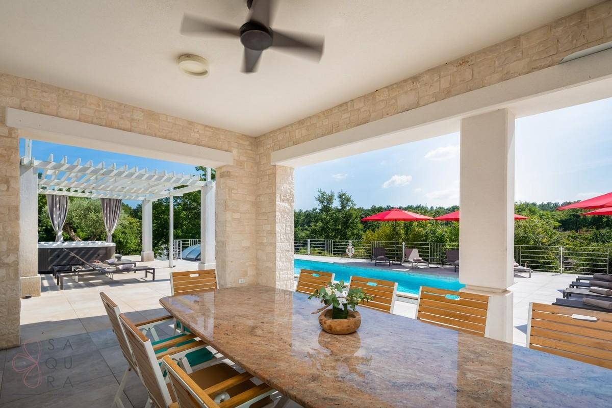 Überdachter Essbereich im Freien mit Blick auf den Pool und den Whirlpool unter einer Pergola.