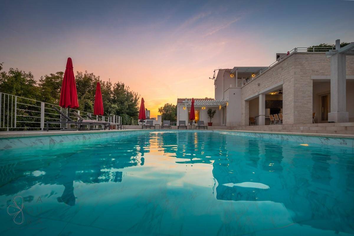 Ruhiger Poolbereich bei Sonnenuntergang mit spiegelnder Wasseroberfläche und Hausfassade im Hintergrund.