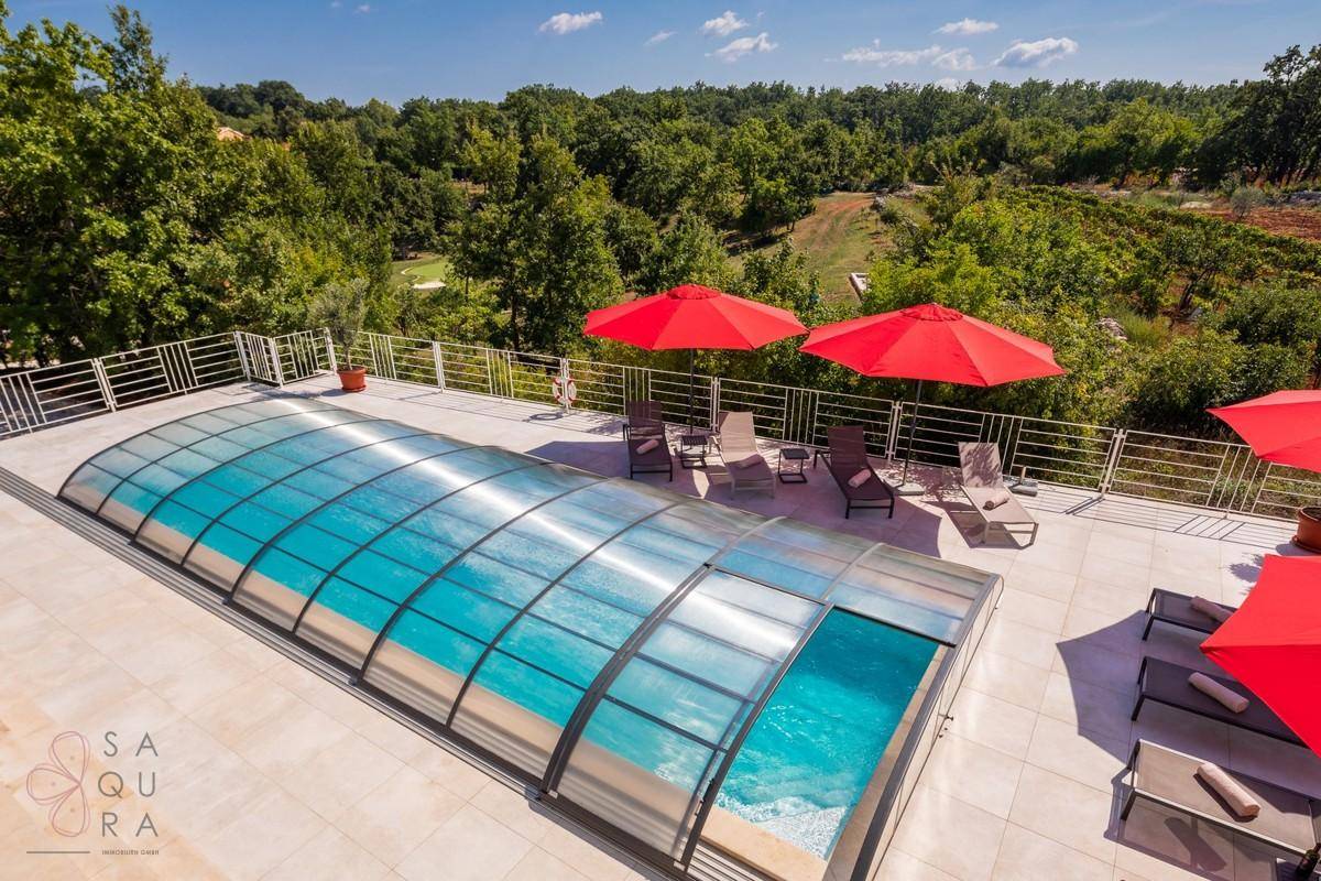 Poolbereich mit teilweiser Überdachung und Liegestühlen, umgeben von grüner Landschaft und Fernblick.