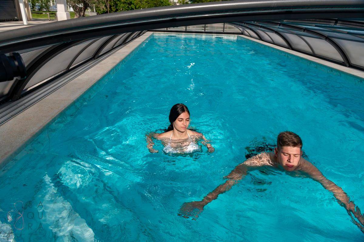 Zwei Personen genießen ein Bad im überdachten Pool mit klarem, blauem Wasser.
