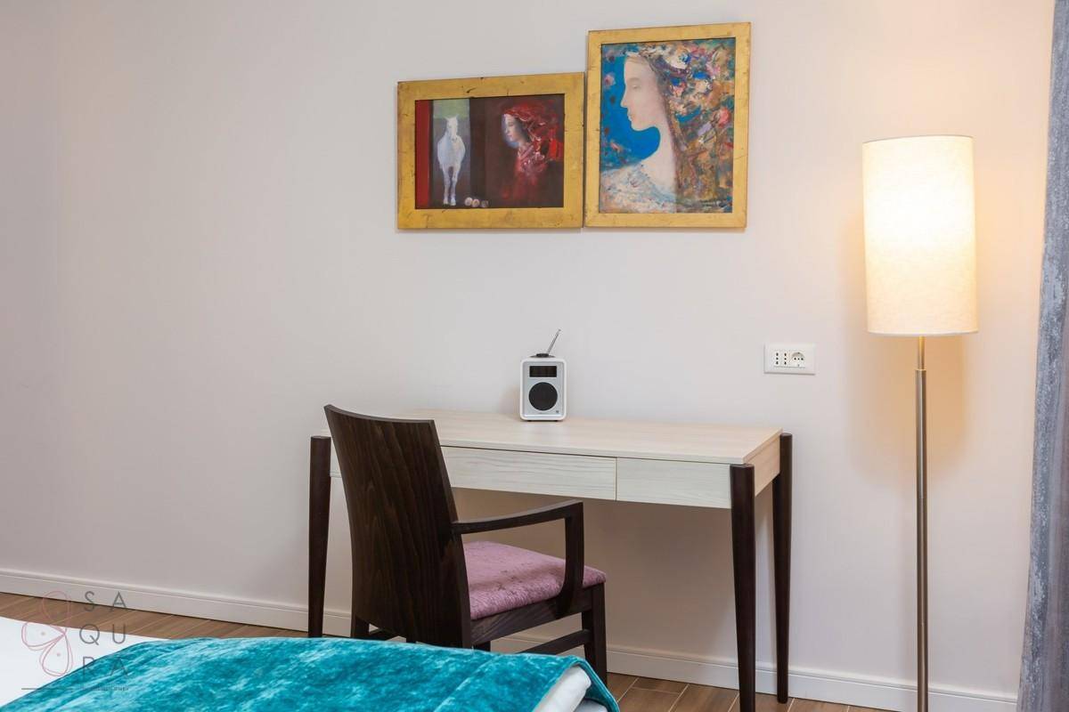 Detailansicht eines Schreibtisches im Schlafzimmer mit moderner Lampe und Kunstwerken an der Wand.