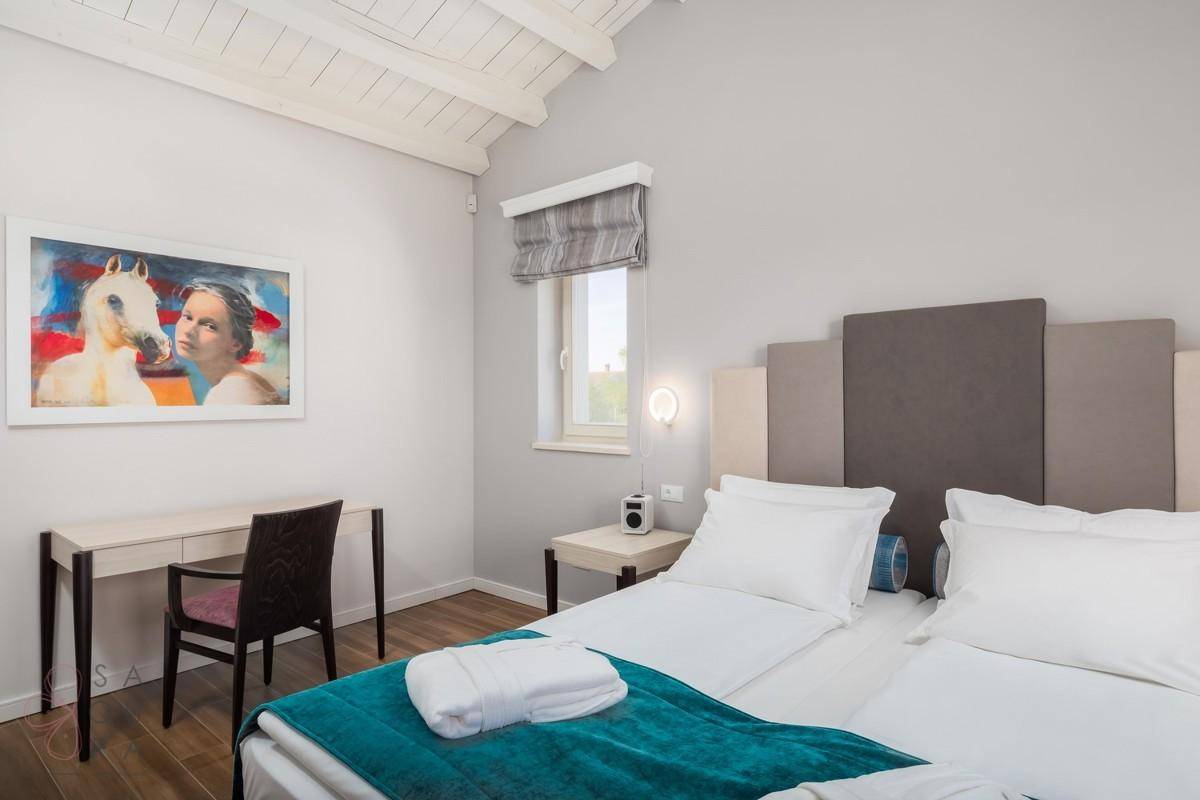 Helles Schlafzimmer mit Holzbalkendecke, Schreibtisch und modernem Kunstwerk an der Wand.