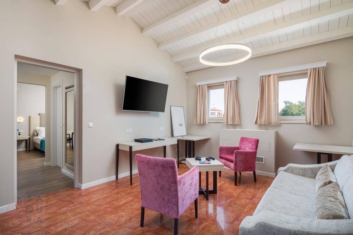Geräumiges Wohnzimmer mit Holzbalkendecke, Wandfernseher und bequemen Sitzgelegenheiten.