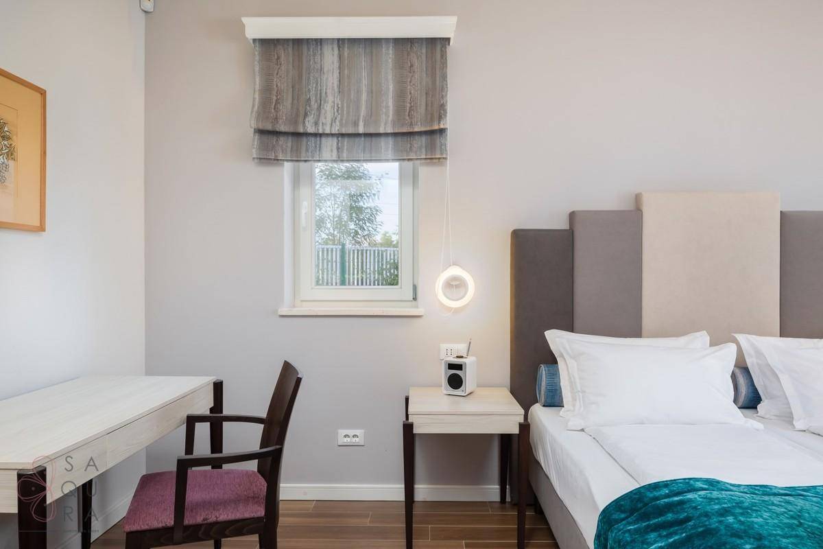 Gemütliches Schlafzimmer mit Schreibtisch, Holzbalkendecke und moderner Beleuchtung am Bett.