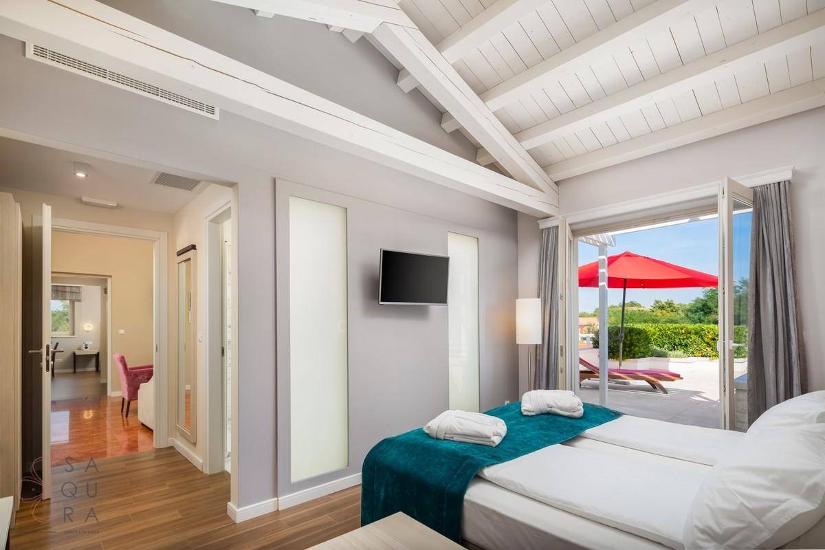 Schlafzimmer mit Holzbalkendecke, Wandfernseher und Blick auf den Poolbereich.