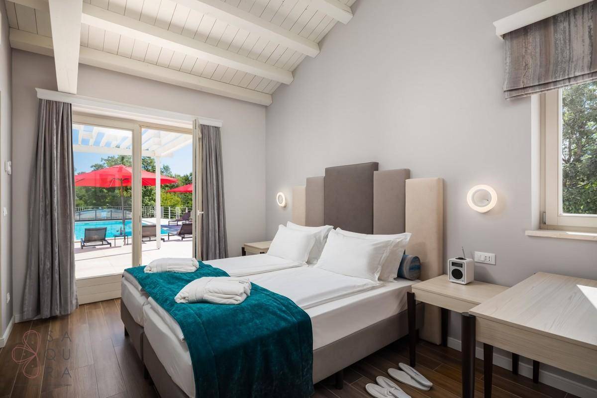 Schlafzimmer mit Holzbalkendecke, zwei Einzelbetten und direktem Blick auf den Poolbereich.