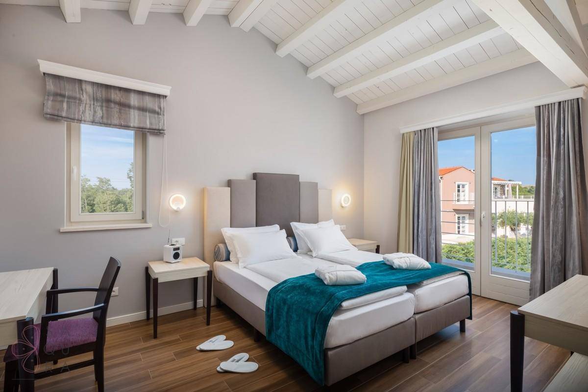 Helles Schlafzimmer mit Holzbalkendecke, zwei Einzelbetten und direktem Balkonzugang.