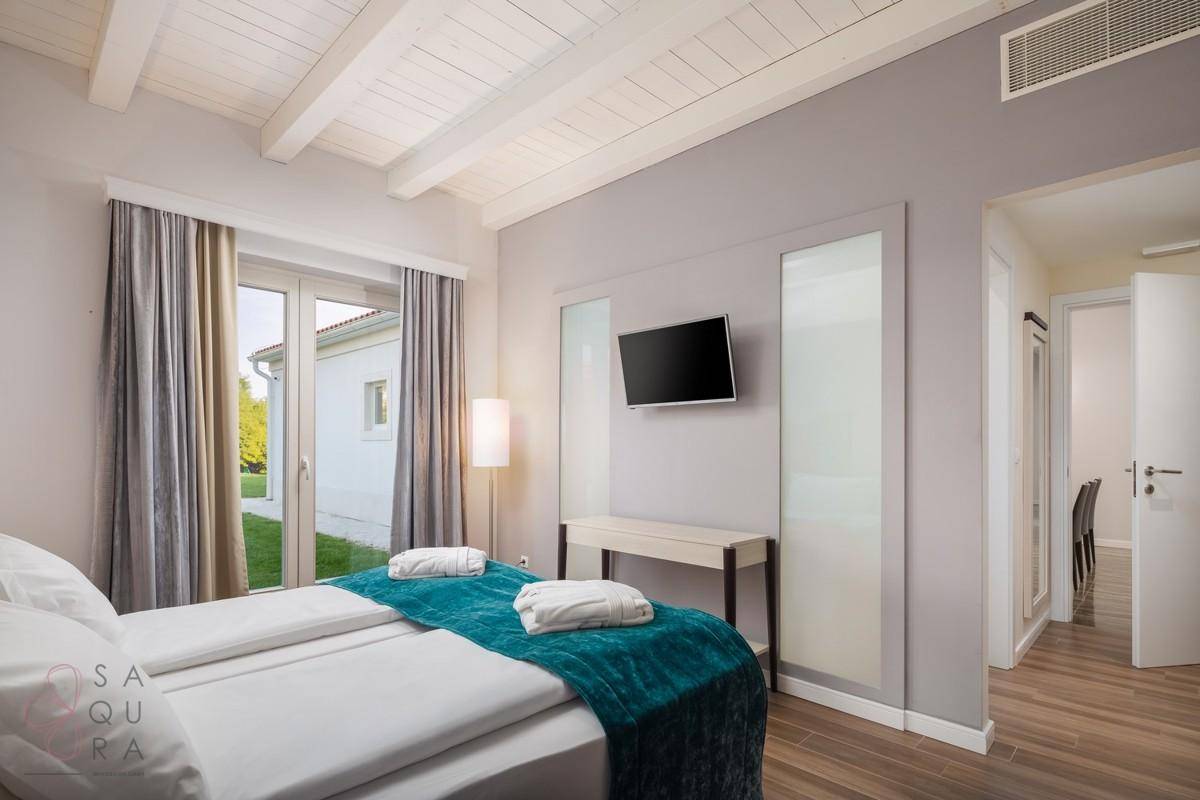 Schlafzimmer mit Holzbalkendecke, Wandfernseher und Zugang zu einem weiteren Wohnbereich.