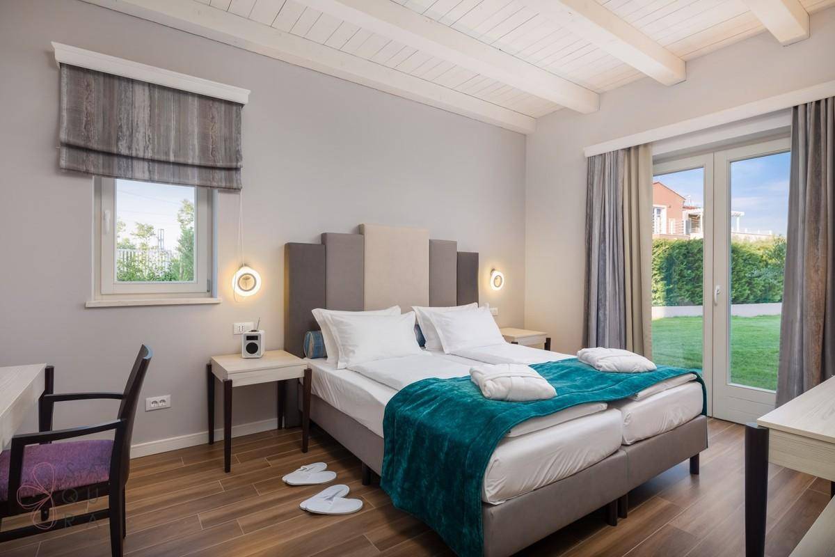 Helles Schlafzimmer mit Holzbalkendecke, zwei Einzelbetten und Zugang zum Gartenbereich.