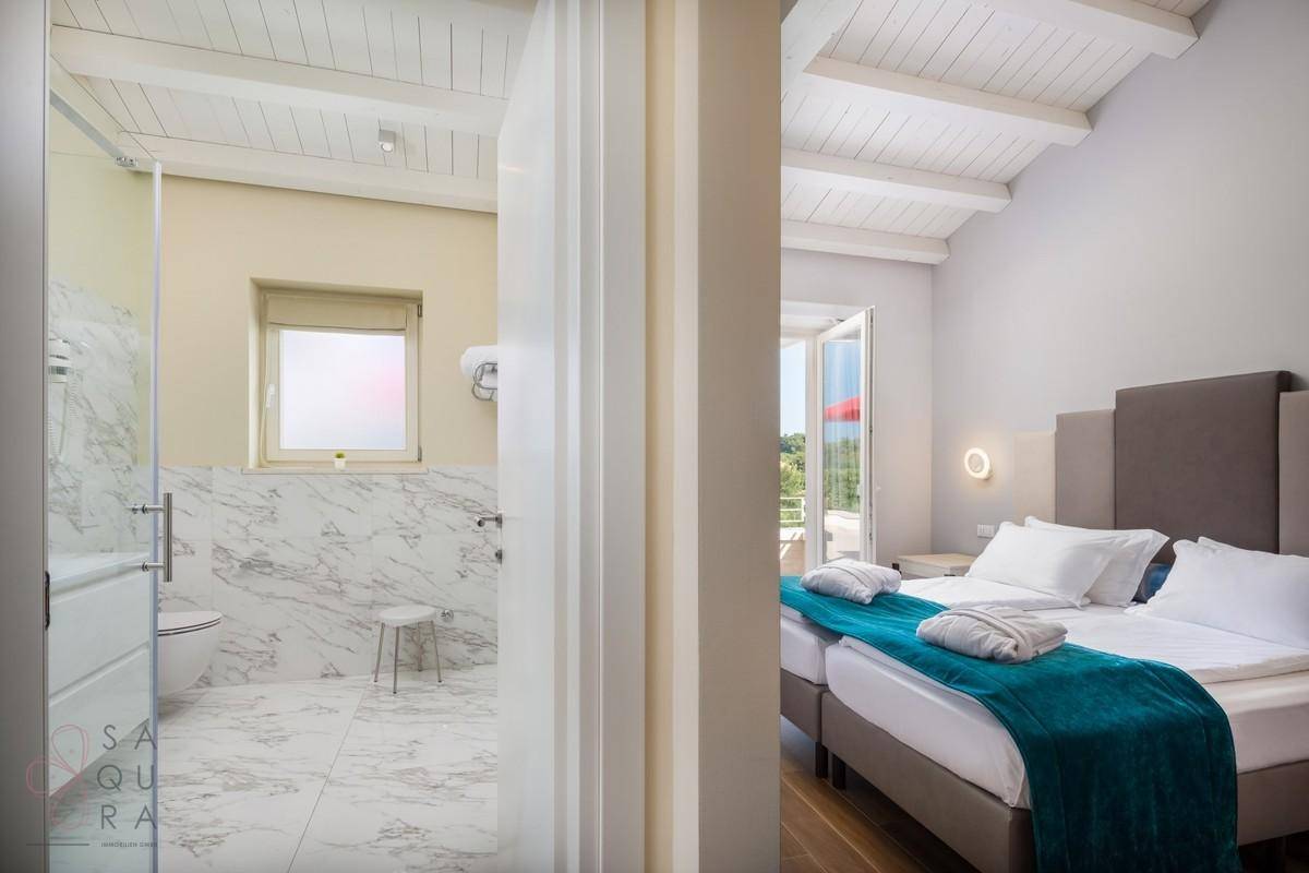 Schlafzimmer mit Holzbalkendecke und angrenzendem Badezimmer mit eleganten Marmorfliesen.