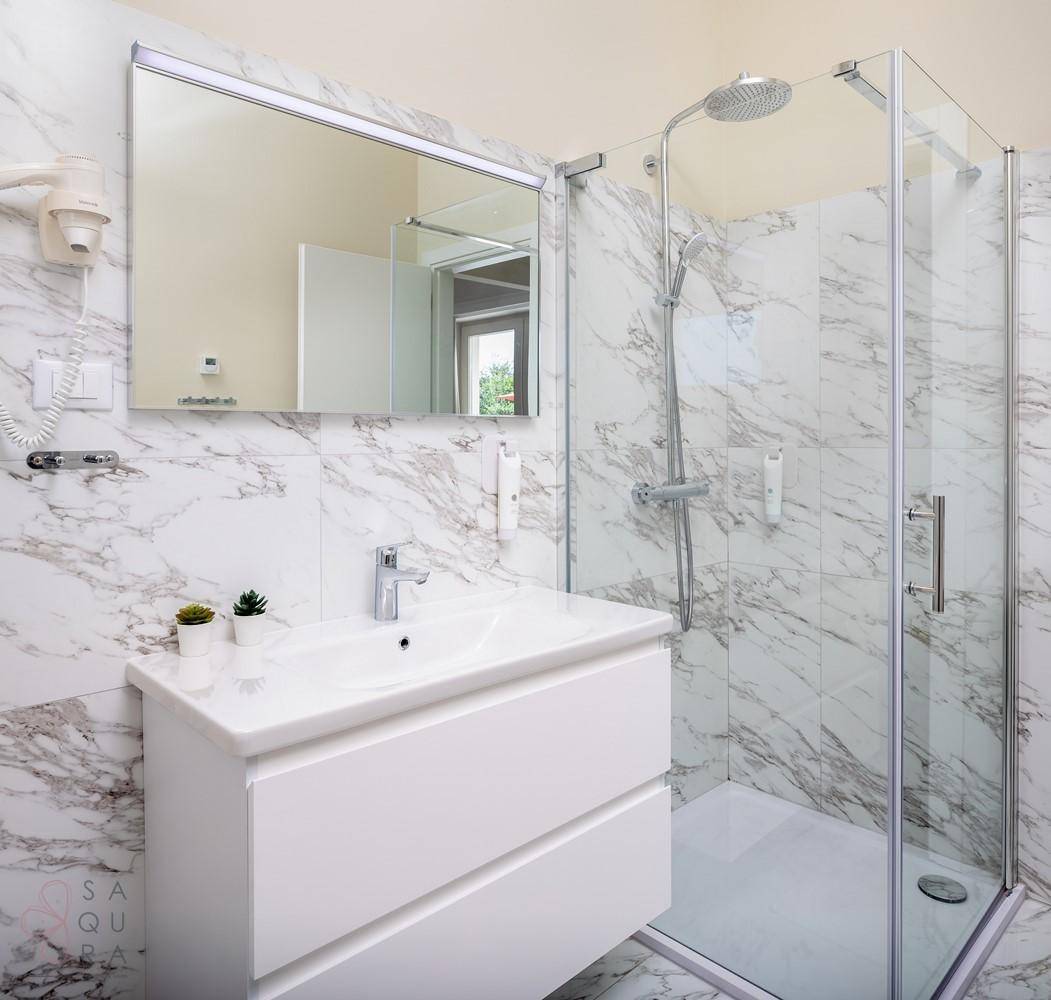 Modernes Badezimmer mit Marmorfliesen, Einzelwaschbecken und einer geräumigen Glasdusche.