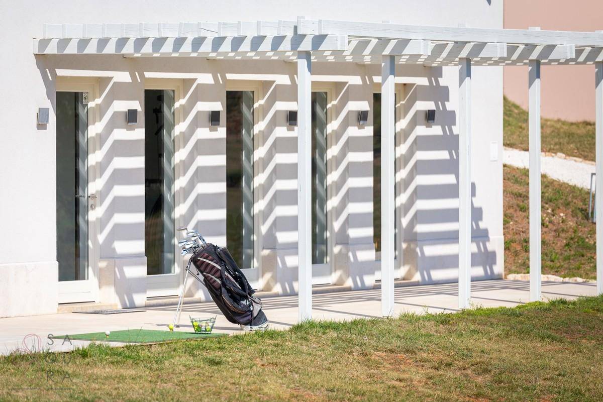 Weiße Pergola vor dem Gebäude mit großen Fenstertüren und Golfschläger-Set.