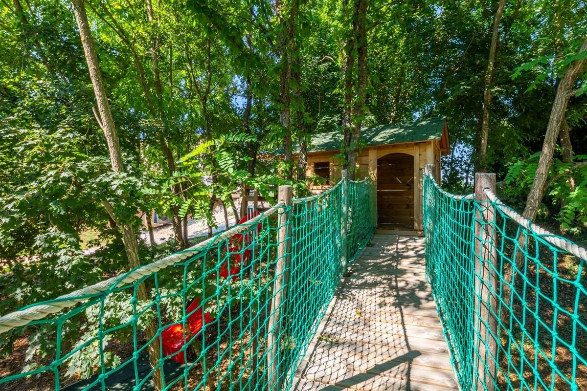 Hängebrücke mit Netzgeländer führt zu einem Baumhaus in einem grünen Wald.