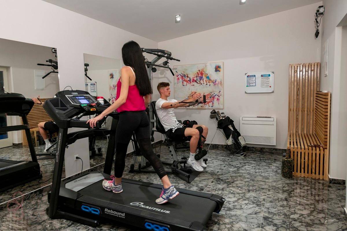 Fitnessraum mit Laufband, Trainingsgeräten und glänzendem Marmorboden.