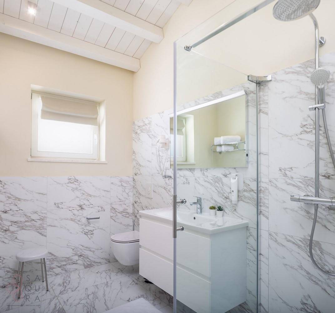 Modernes Badezimmer mit Marmorfliesen, ebenerdiger Dusche und Fenster für Tageslicht.