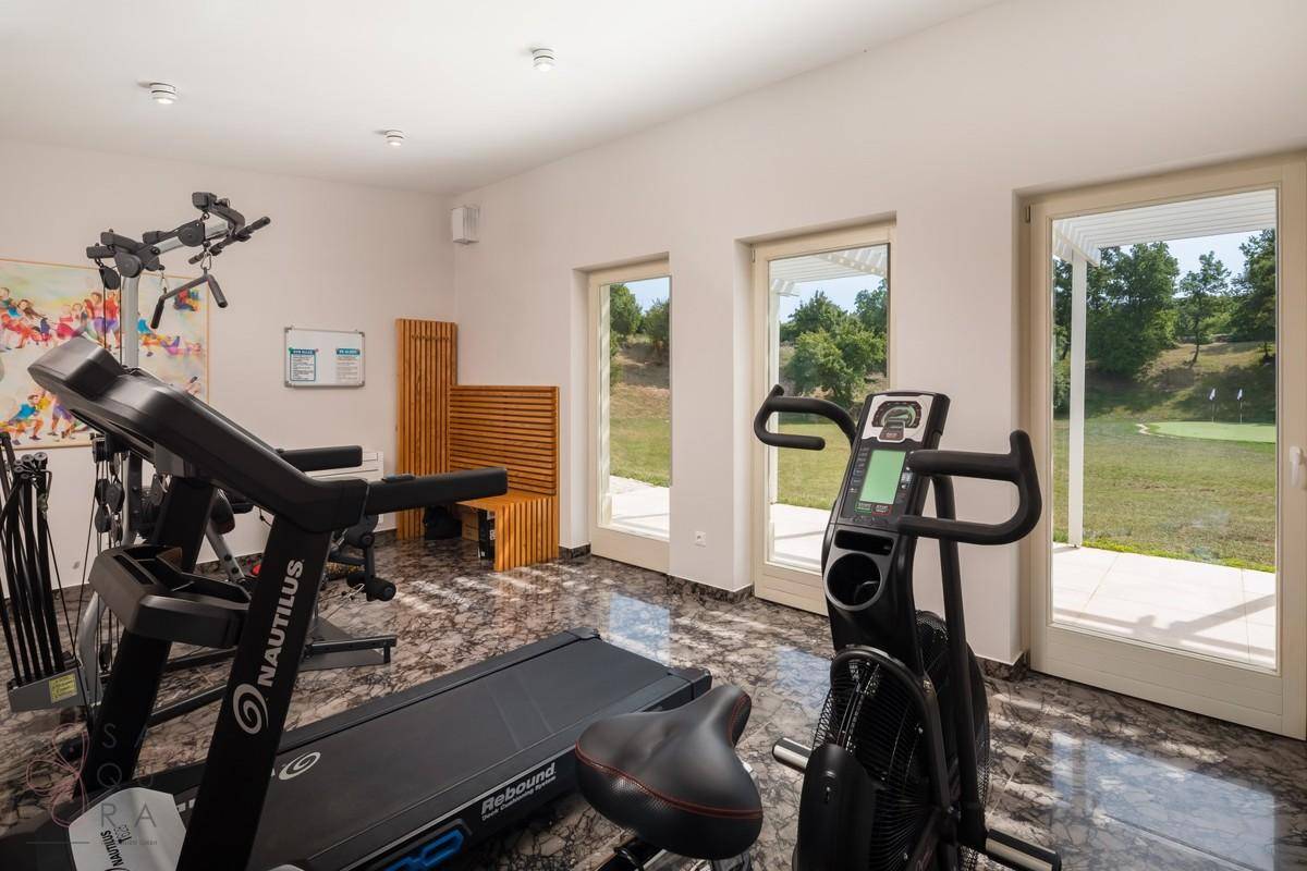 Heller Fitnessraum mit verschiedenen Trainingsgeräten und Zugang zum Außenbereich.