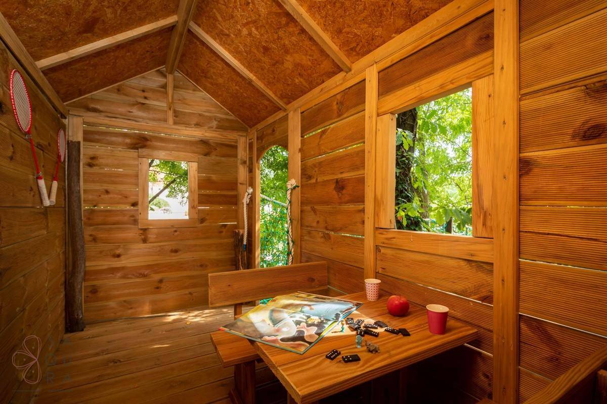 Rustikales Baumhaus-Interieur mit Holzwänden, Tisch und Brettspielen für Unterhaltung.