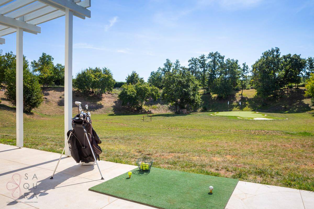 Überdachter Bereich für Golfübungen mit Blick auf das Putting-Green und die weite grüne Landschaft.