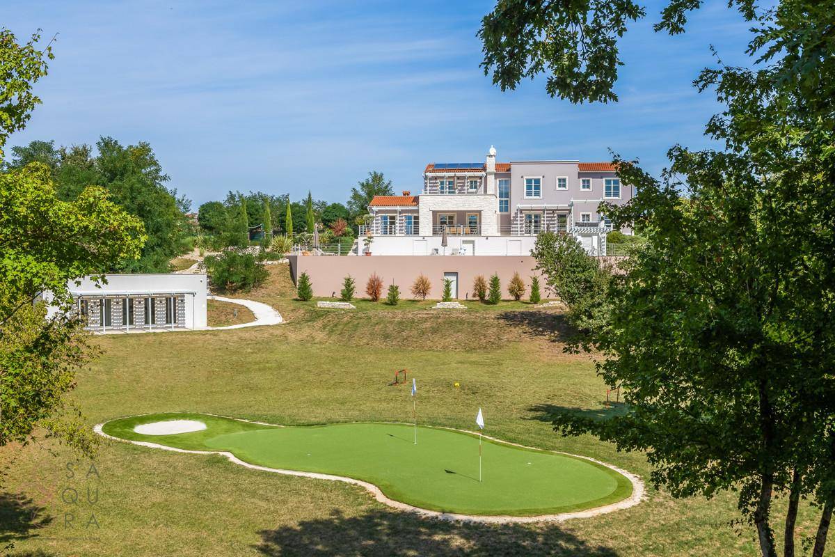 Moderne Villa mit Blick auf ein Golf-Putting-Green und die umliegende grüne Hügellandschaft.