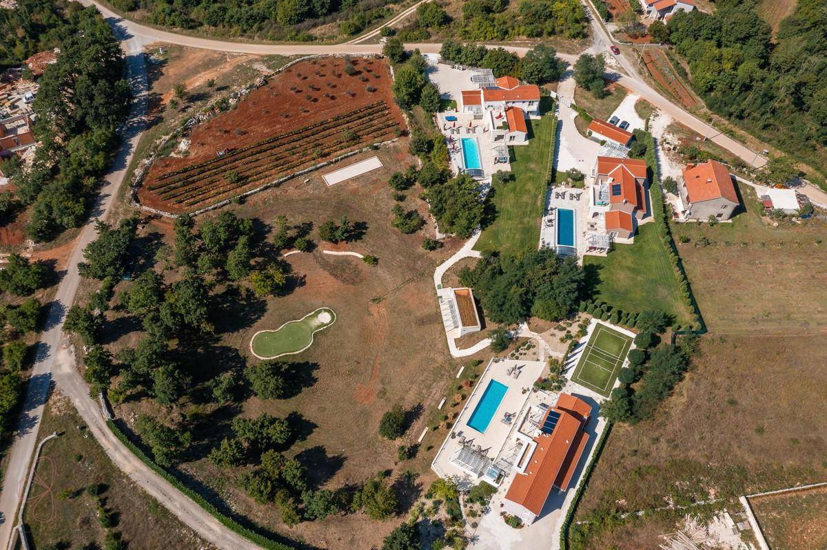 Panoramablick aus der Luft auf das weitläufige Anwesen mit Villen, Pools, Tennisplatz und umgebender Natur.